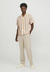Kortarmig, knoopsluiting overhemd met horizontale strepen in wit en lichtbruin; gecombineerd met beige broek en witte sneakers.