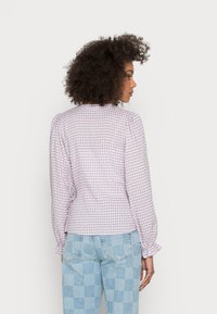 Blusa quadriculada em roxo e branco com mangas bufantes, punhos franzidos e um decote redondo, combinada com jeans quadriculados em azul claro.