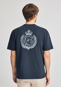 Mörk marinblå bomull t-shirt med en stor vit logo på ryggen, prydd med en krona och lagerblad. Kortärmad, avslappnad passform.