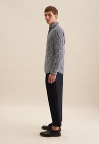 Camicia abbottonata con un motivo floreale blu navy, abbinata a pantaloni neri su misura e scarpe nere, rappresentata da una vista laterale su uno sfondo neutro.