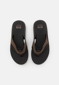Brune flip-flops med en teksturert svart fotbed, gummisåle og stofftanga. Har kontrasterende sømmer og logodetalj.
