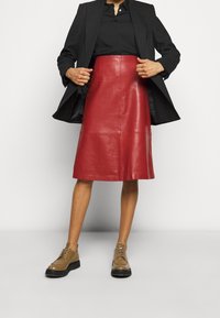 Falda midi de cuero rojo con una textura suave y un corte recto, combinada con un blazer negro y zapatos cordones marrones.