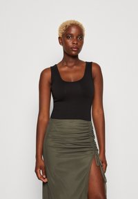 Black sleeveless top paired with a green ruched skirt featuring a thigh-high slit and tie detail, made from soft, lightweight fabric.
