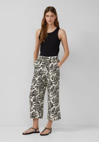 Un haut noir sans manches associé à un pantalon large à jambes larges avec un motif de feuilles noir et blanc. Des sandales complètent la tenue.