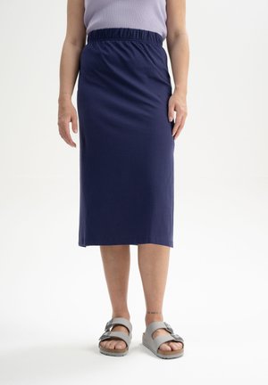 Donkerblauwe, knielange rok met een elastische tailleband, gemaakt van zachte stof. Gecombineerd met grijze sandalen met een gespsluiting.