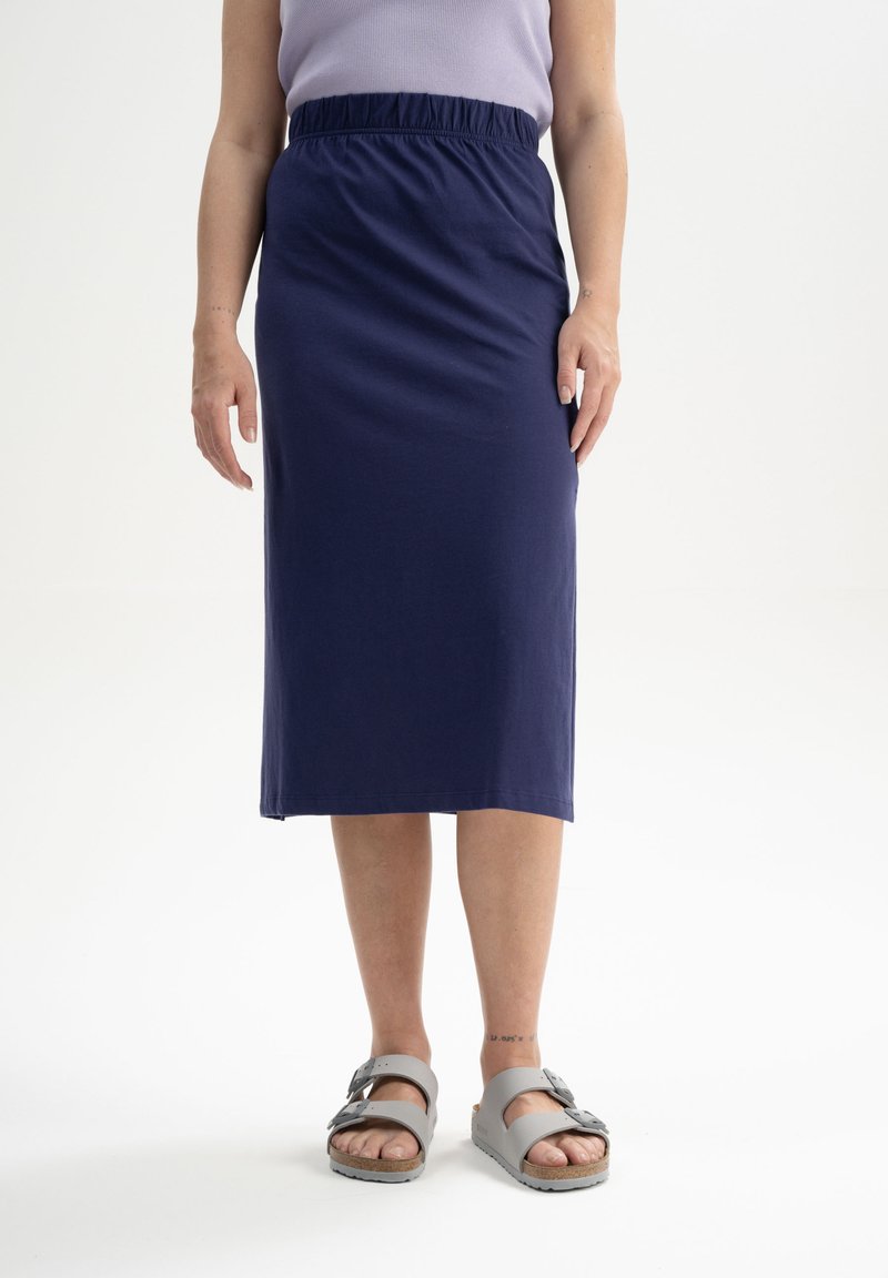 Donkerblauwe, knielange rok met een elastische tailleband, gemaakt van zachte stof. Gecombineerd met grijze sandalen met een gespsluiting.