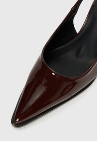 Scarpa slingback in pelle verniciata bordeaux con punta affusolata, caratterizzata da una texture liscia e un design minimalista, che presenta un interno nero e cuciture sottili.