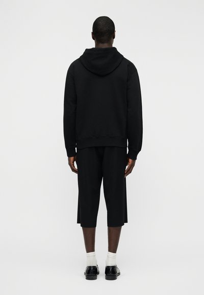 Μαύρο φούτερ με κουκούλα και υφή, με κουκούλα και ριμπ μανσέτες. Συνδυασμένο με μαύρο cropped παντελόνι και μαύρα παπούτσια. Απλή, μονοχρωματική εμφάνιση.