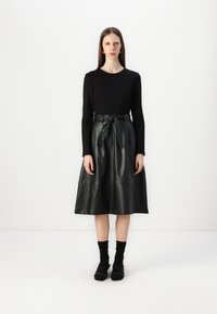 Top negro de manga larga combinado con una falda de cuero negro de corte A y cintura alta, que presenta un cinturón atado y una textura suave, con un acabado mate.