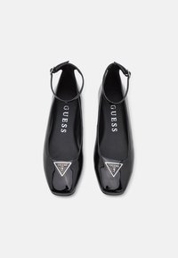 Balerini din piele patent neagră, cu vârf pătrat, curea la gleznă și logo triungiular argintiu în față; textură netedă și design modern.