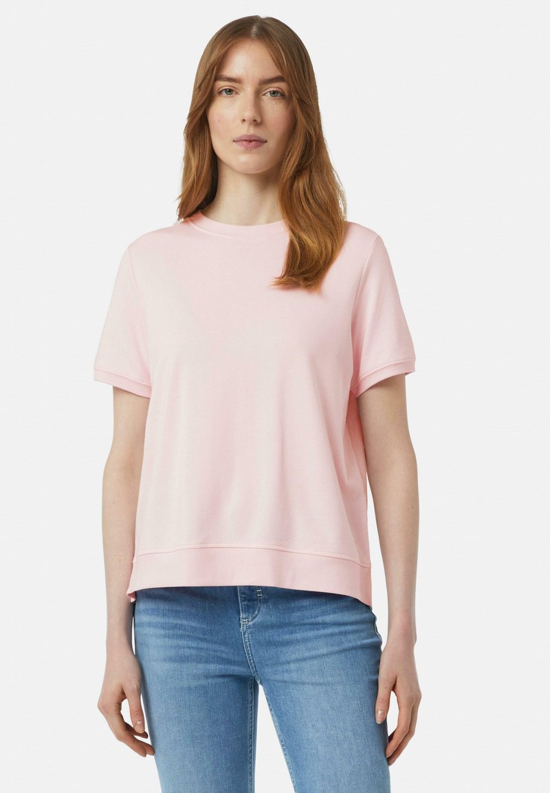 Lichtroze, kortek mouwen, crew-neck t-shirt gemaakt van zachte stof met een ontspannen pasvorm, met een geribde halslijn en zoom. Draagt bij blauwe jeans.