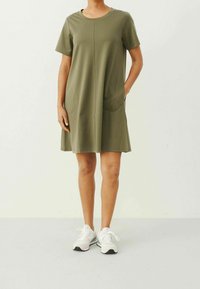Vestido verde oliva de manga corta con escote redondo, dos grandes bolsillos frontales y un corte relajado; hecho de una tela suave y lisa.