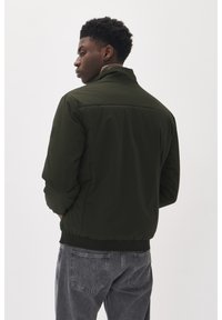 Dunkelgrüne Bomberjacke mit Stehkragen, elastischen Bündchen und Saum. Glattes Material mit einem kleinen Logo-Detail am linken Ärmel.