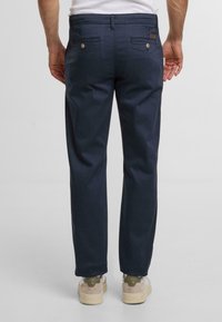 Granatowe spodnie o gładkiej teksturze, z dwoma tylnymi kieszeniami i subtelnym logo przy pasie.