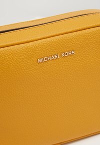 Gul pebret læderhåndtaske med rektangulær form. Et metallisk "Michael Kors" logo er synligt på fronten. Tekstur overflade detalje.