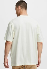 Lyscremet kortærmet t-shirt i afslappet pasform, med rund hals og blød tekstur. Syning ved kanterne og minimal detaljer synlige.