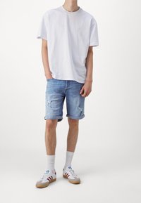 Bílá bavlněná tričko, světle modré džíny kraťasy s ohrnutými lemy, neformální šedé a bílé tenisky s červenými pruhy a bílé kotníkové ponožky.