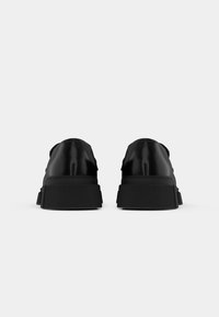 Black sneakers with a smooth, shiny upper, featuring a textured rubber sole and minimalist design. No visible logos or patterns.