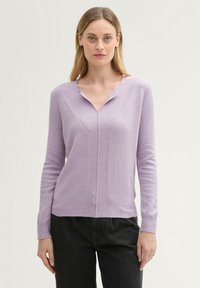 Lila trui met een V-hals, lange mouwen en een gestructureerde voorkant. Beschikt over verticale ribbels en een aansluitende pasvorm. Gepaard met zwarte broek.