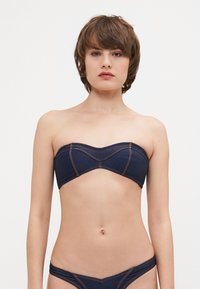 Denim bikini vrh s bandeau dizajnom, temno modre barve in kontrastnimi oranžnimi šivi. Prilegajoč in brezšiven okoli prsi.