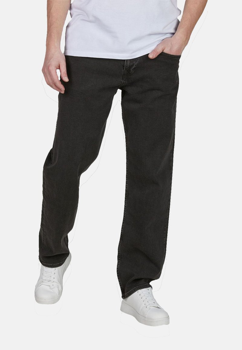 Jeans de mezclilla negra con un diseño de pierna recta, cinco bolsillos y detalles de costura clara, combinados con zapatillas blancas y una camiseta blanca.