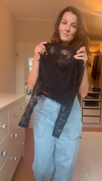 Schwarzes Spitzenoberteil mit transparenten Details und langen Ärmeln, vor einem hellen Hintergrund präsentiert. Kombiniert mit hellblauen Jeanshosen.