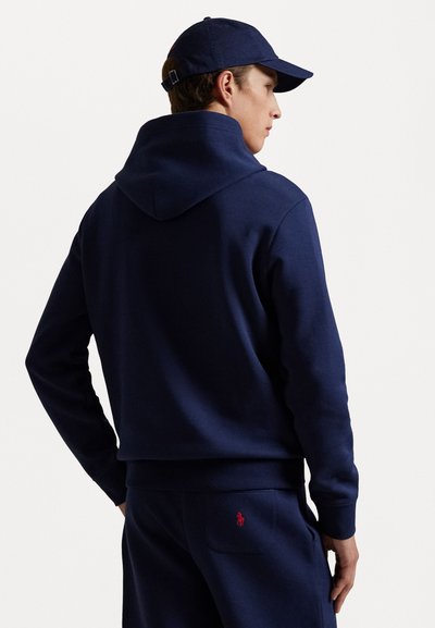 Sudadera azul marino con capitán ajustable y puños acanalados, combinada con pantalones a juego que tienen un pequeño logotipo bordado en el bolsillo trasero.