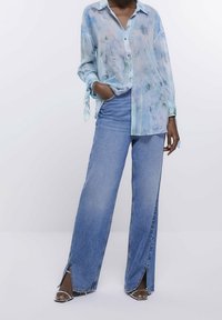Light blue, flowing button-up shirt with a floral pattern; paired with wide-leg, distressed blue denim jeans featuring side slits.