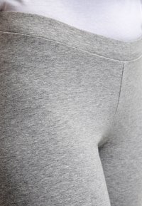 Närbild av ljusgrått åtsittande tyg, troligtvis leggings eller byxor, som bärs över ett vitt plagg vid midjan.