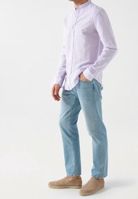 Lichtpaarse lange mouwen shirt met een bandkraag, gecombineerd met lichtblauwe jeans en beige instapschoenen. Casual outfit met een relaxte pasvorm.