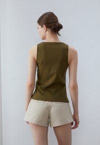 Oliven grønn ermeløs topp laget av mykt stoff, tettsittende design, parret med lyse beige shorts. Minimalistisk stil, ingen synlige mønstre eller detaljer.