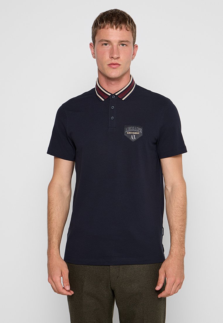 Navy blauwe polo shirt van katoen, met een gestreepte kraag, een knoopsluiting met drie knopen en een logo patch op de linkerborst.
