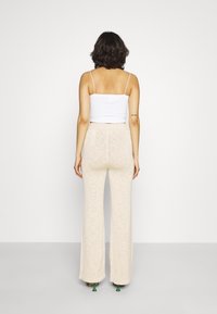 Calças largas de malha bege e um top cropped branco com textura canelada. As calças têm um acabamento texturizado e assentam alto na cintura, com um cós oculto.