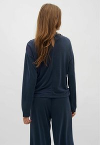 Námornícky modrý dlhý rukáv s detailom na drapérii vzadu, vyrobený z jemnej látky, skombinovaný s rovnako ladenými nohavicami, minimalistický dizajn, hladká textúra.