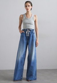 Φαρδιά τζιν παντελόνια σε ξεθωριασμένο μπλε χρώμα, με ψηλή μέση και κλείσιμο με κορδόνι, συνδυασμένα με μια εφαρμοστή γκρι εμφανισιακή μπλούζα.