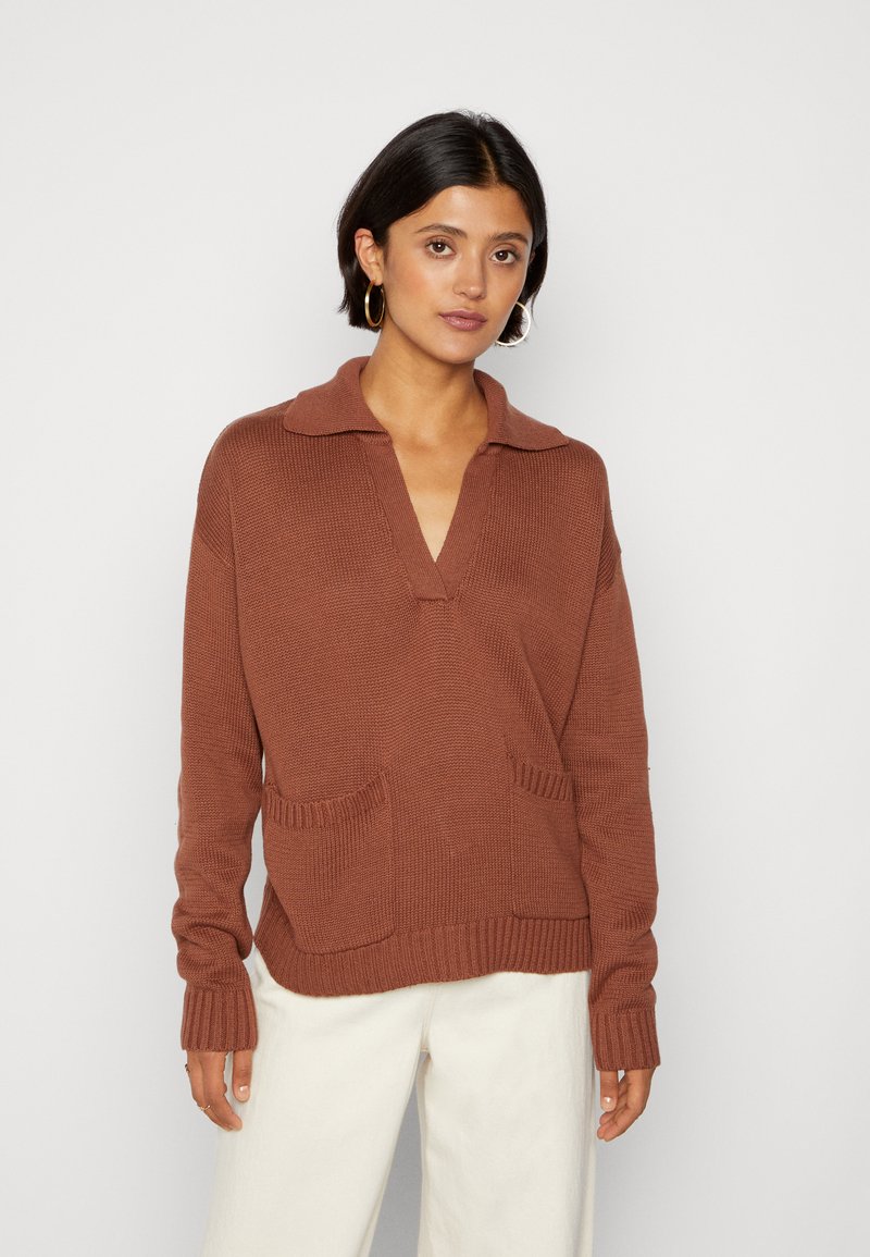 Brun strikket sweater med V-hals og krave, udstyret med to frontlommer og ribbede manchetter. Glat tekstur og afslappet pasform.