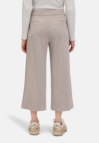 Beige levelekav trousers dengan kain bertstruktur, pinggang pas, dan dua saku belakang, dipadukan dengan sepatu sneaker beige.