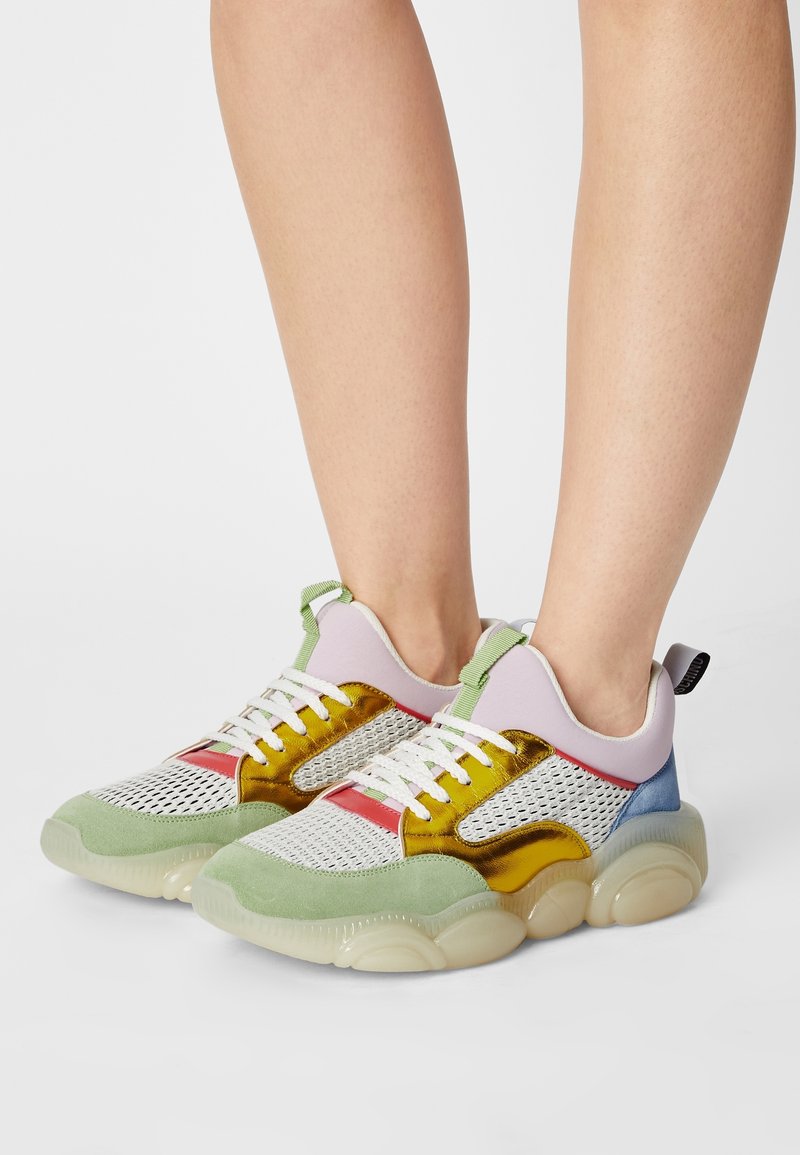 Des sneakers colorés en mesh et en suède, avec un mélange d'accents verts, dorés, roses et bleus, et une semelle chunky translucide.