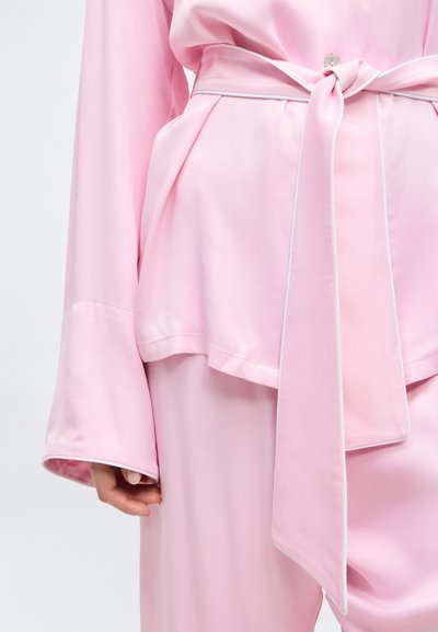 Απαλή ροζ σατέν μπλούζα με φαρδιές μανσέτες και ταιριαστό παντελόνι, με ζώνη που δένει στη μέση και έχει λευκή επένδυση.