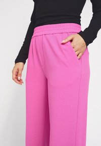 Roze, wijde broek van zacht materiaal, met een elastische tailleband en zijzakken. Glad textuur met een uniforme kleur.