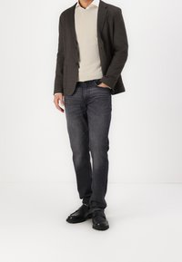 Grijze blazer over een crèmekleurige trui, donkere jeans en zwarte schoenen. De blazer heeft een gladde textuur en de jeans hebben een subtiele vervaagde patroon.