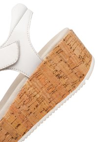 White leather sandal with a cork wedge sole. Features a rounded, open design, adjustable strap, and textured cork pattern on the heel.