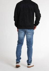 Czarna zamszowa kurtka bombowa z prążkowanymi mankietami i dołem, w połączeniu z jasnoniebieskimi dżinsami. Białe sneakersy z czarnymi i brązowymi akcentami.