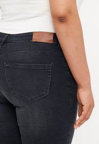 Dark denim jeans with a slim fit, featuring a leather patch at the back waist and two back pockets with subtle stitching details.