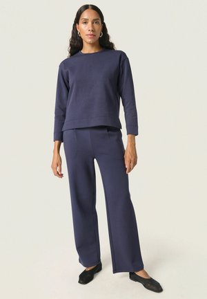 Mørkeblå loungewear sæt bestående af en langærmet top med lige snit og matchende brede bukser, lavet af blødt stof.
