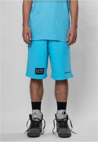 Turkise treningsshorts med elastisk midje, med en svart label på venstre lår. Kombinert med grå basketballsko og svarte sokker.