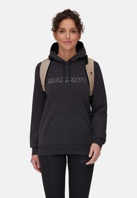 Svart huvtröja med kenguruficka och "MAMMUT"-logotyp i vit sömnad, ihop med svarta texturerade leggings och en beige ryggsäck.