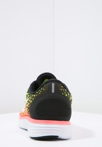 Černá sportovní bota s vícebarevným síťovaným svrškem v žluté a červené barvě, texturovaným podpatkem a růžovými akcenty na bílé podrážce.
