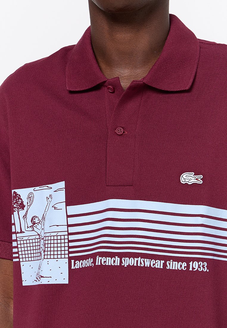 Burgundowa koszulka polo z teksturowanej tkaniny, z białym graficznym motywem tenisisty i poziomymi paskami, logo na klatce piersiowej.