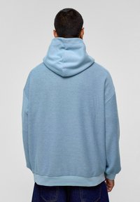 Lichtblauwe hoodie met een gestructureerde afwerking, verlaagde schouders en een ribgebreide zoom, gezien vanuit de achterkant.